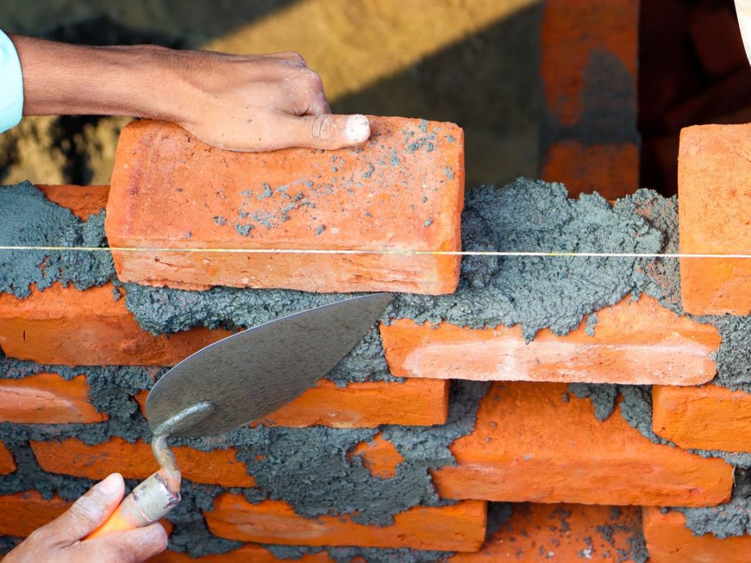 Hände vermauern Ziegel mit Mörtel auf einer Baustelle